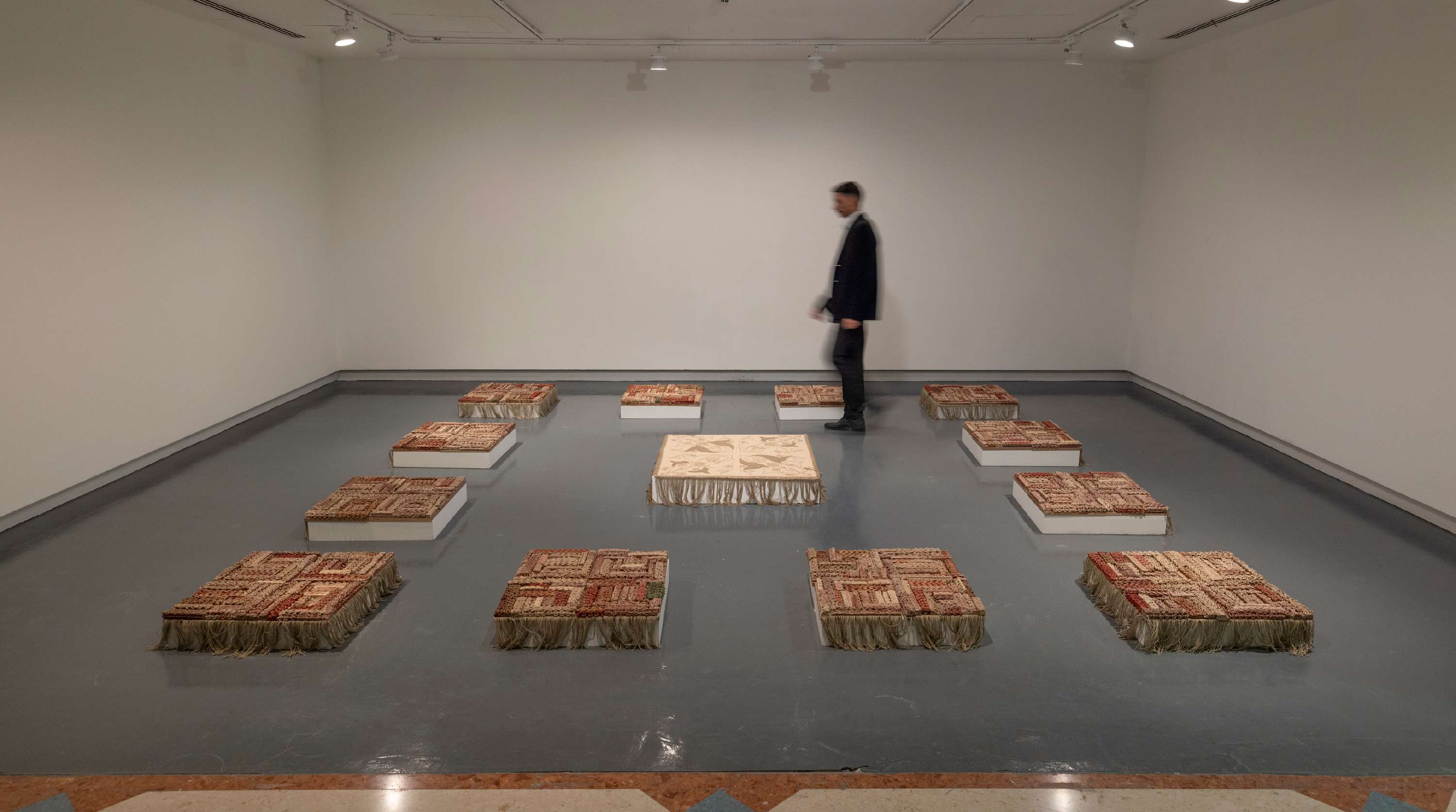 Wide installation view of Before / Pause / After, showing modular ceramic fields arranged around a central textile work